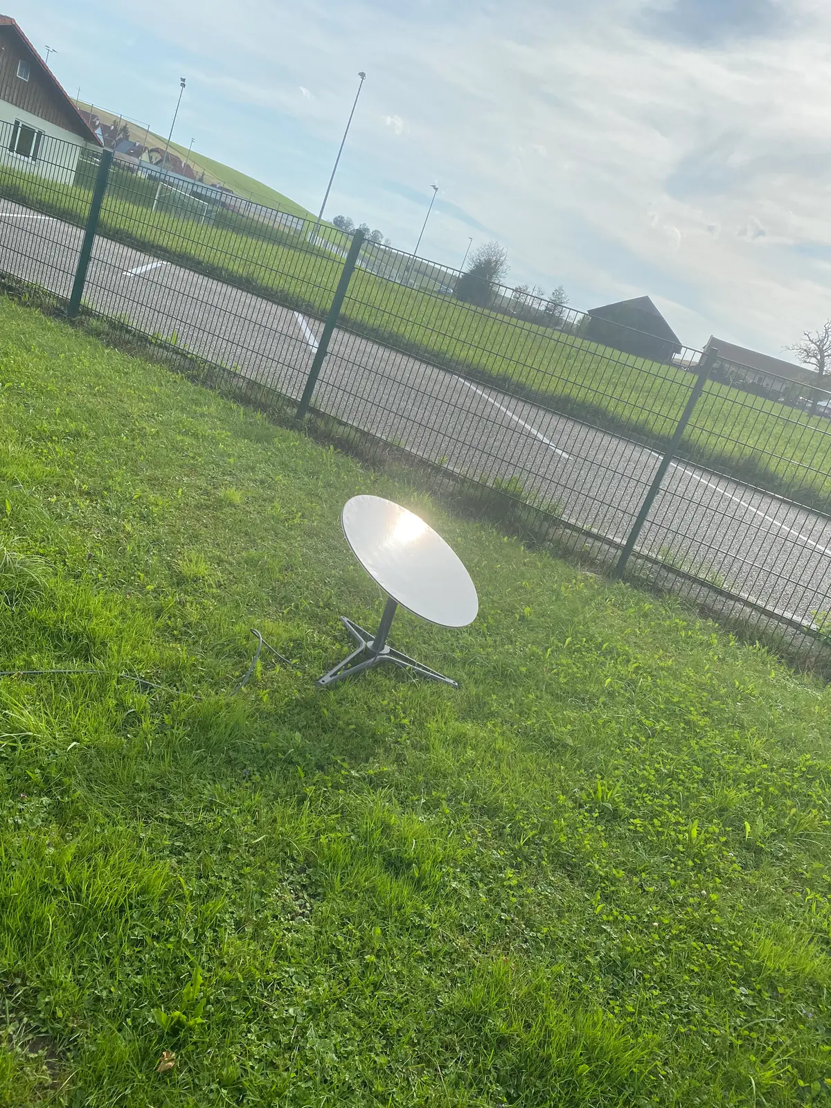 Die runde Starlink-Antenne der ersten Baureihe steht auf ihrem Standfuss im Garten