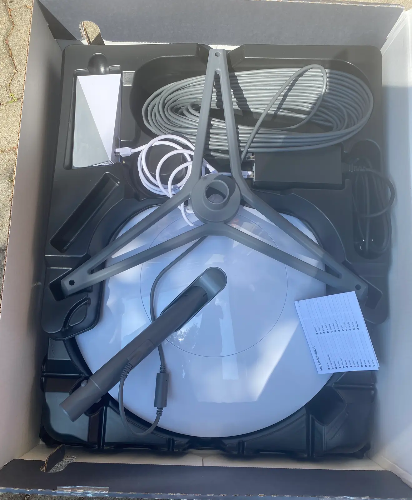 Der geöffnete Versandkarton mit der runden Antenne, dem Standfuss, dem Router und den Kabeln